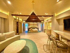 A spacious hotel room with a large bed, a sitting area with a sofa and chairs, a dining table, and a view of the outdoors. - Hotel Shibari Tulum (Tulum)