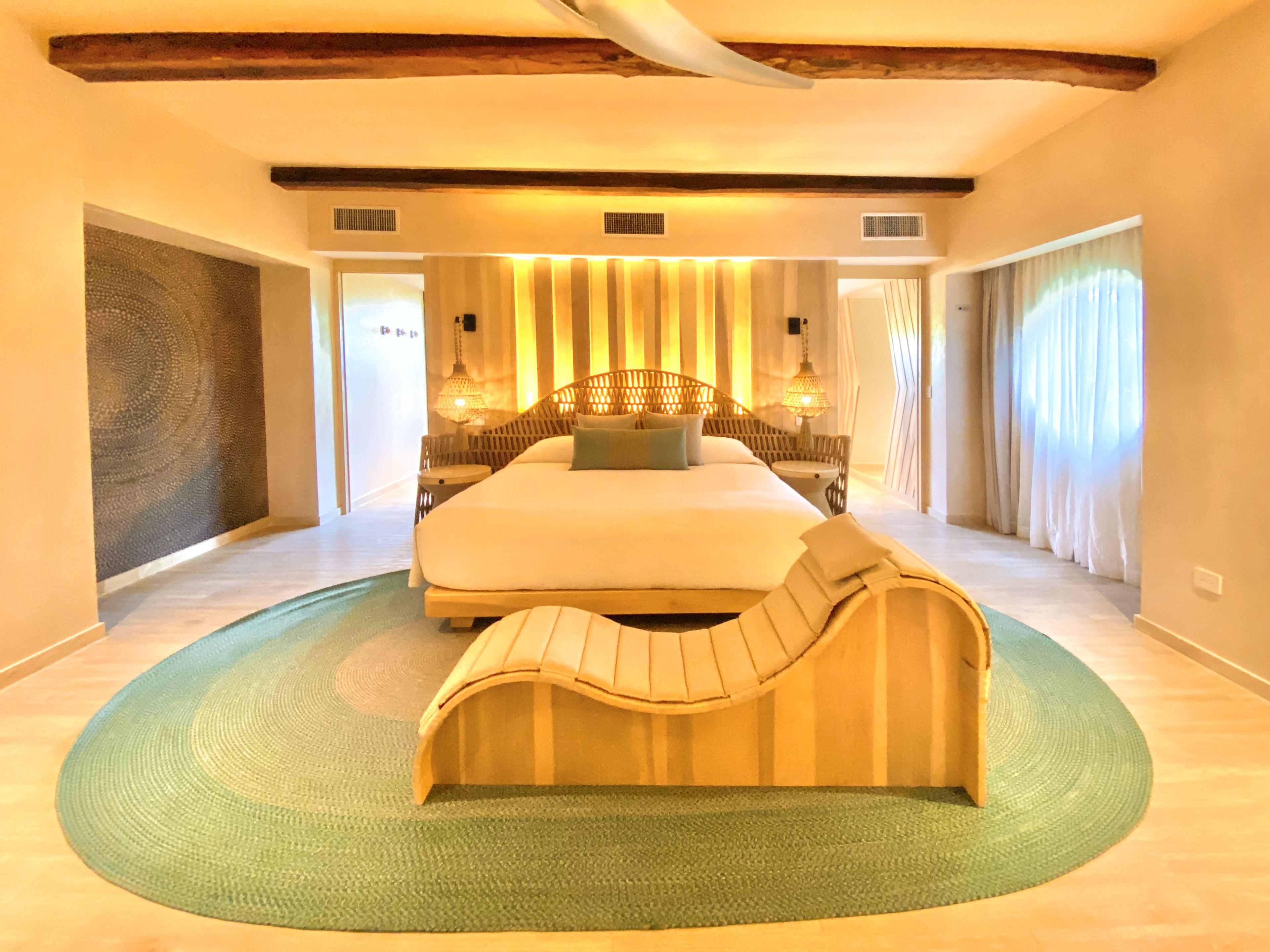A spacious bedroom with a large bed, a curved bench, and a green rug.