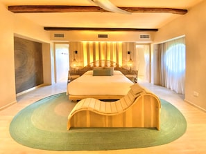 A spacious bedroom with a large bed, a curved bench, and a green rug.