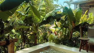 A hot tub surrounded by lush tropical foliage, with a wooden deck and a thatched roof overhead.