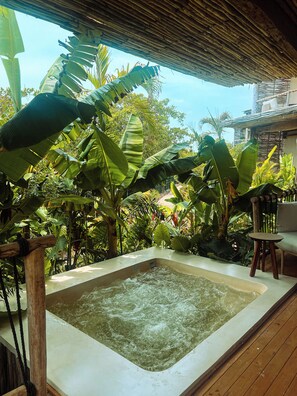 Un bain à remous entouré d’une végétation tropicale luxuriante, avec une terrasse en bois et un toit de chaume au-dessus.