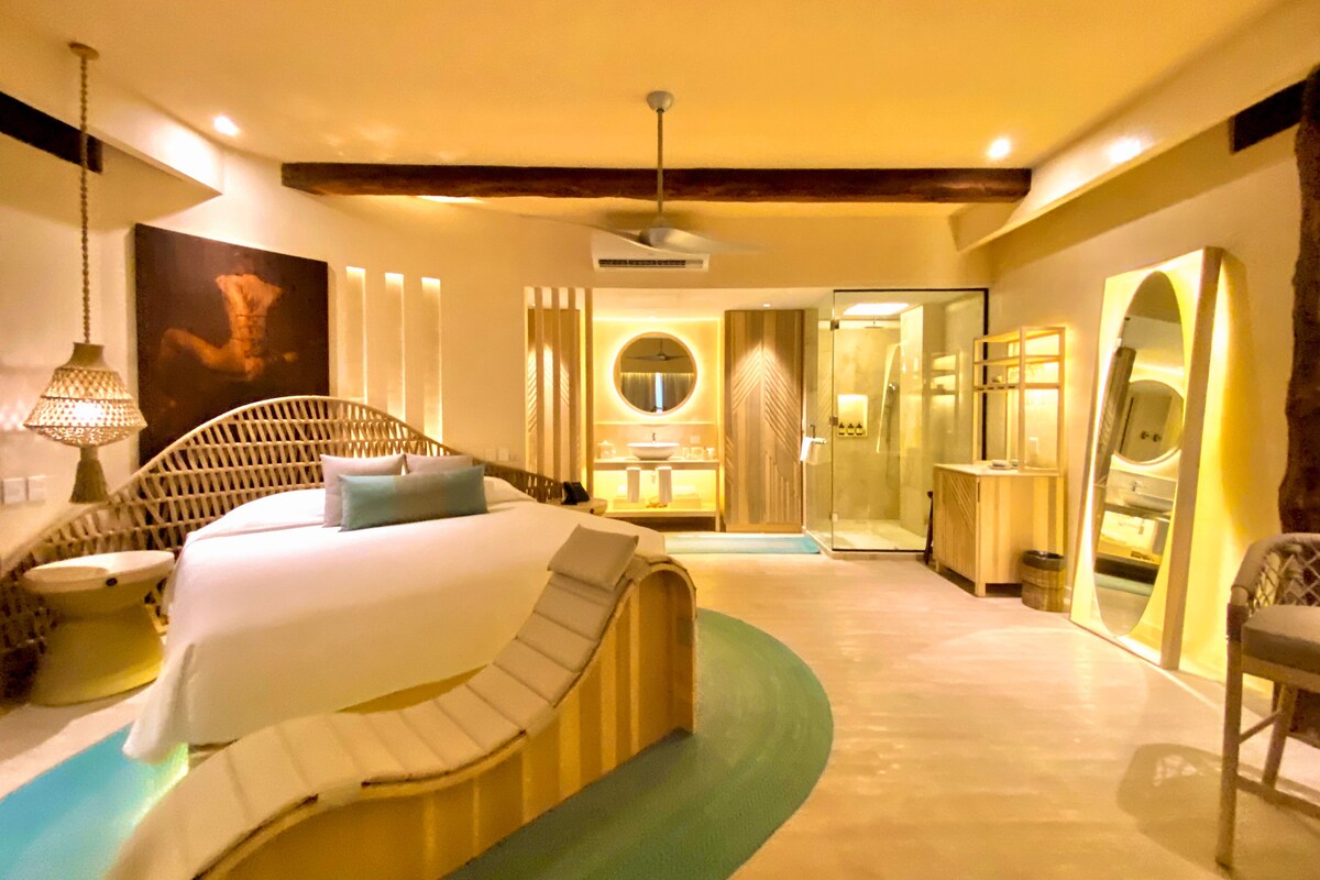 A modern hotel room with a curved bed, a glass shower, and a large mirror.