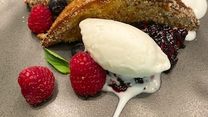Un plat de postre amb dues peces de pastet empanat, maduixes, aranyons i una culleradeta de gelat.
