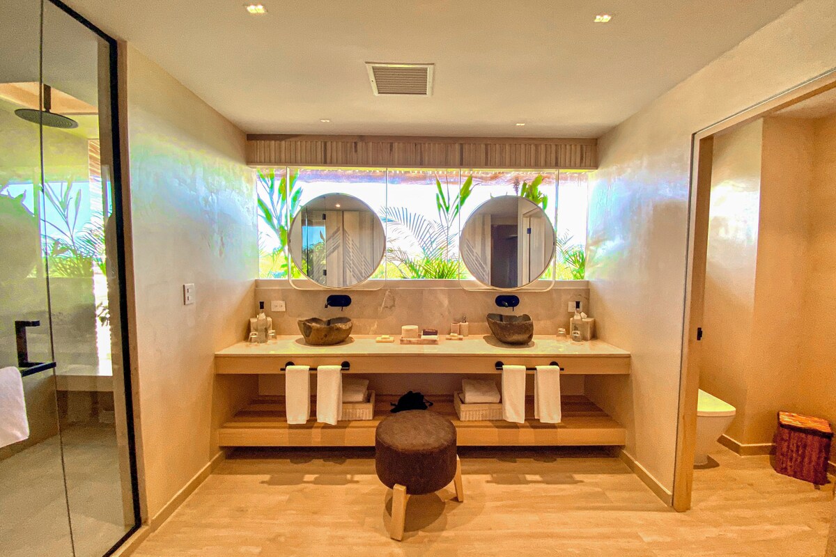 A modern bathroom with a large mirror, two sinks, and a wooden stool.