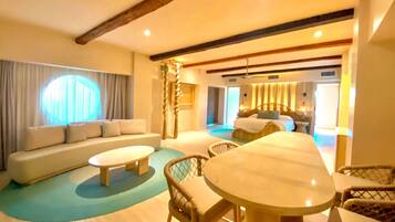 A hotel room with a large bed, a sofa, a dining table, and a seating area with chairs.