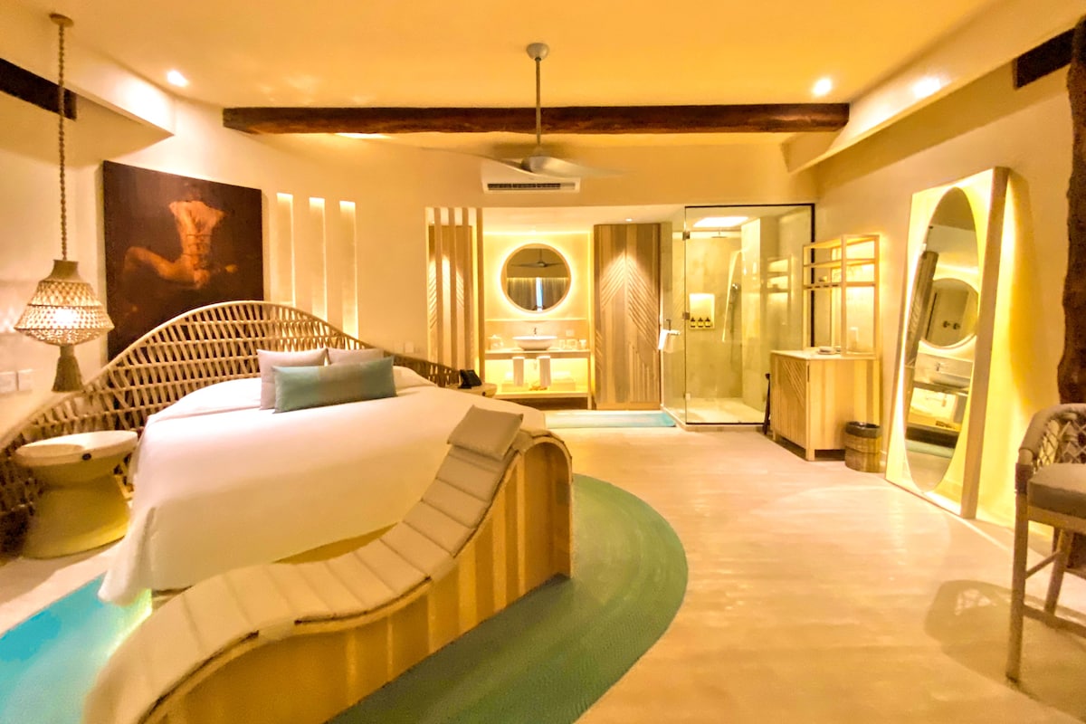 A modern hotel room with a curved bed, a separate bathroom, and a glass shower enclosure.