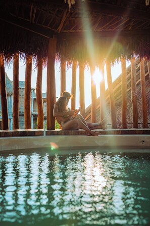 A person sitting by a pool with a thatched roof overhead. - Hotel Shibari Tulum (Tulum)