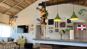 Een rustiek interieur met zichtbare houten balken, een bar met flessen en een aan de muur bevestigde televisie.