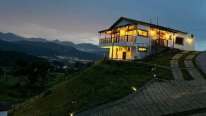 Een huis met twee verdiepingen, met een balkon, gelegen op een heuvel met uitzicht op verre bergen en een stad.