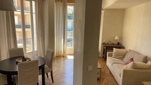 A spacious living room with a wooden herringbone floor, a round dining table with chairs, a sofa, and a view of a balcony through large windows. - Nice 56m² with balcony in rotunda near the sea (Nice)
