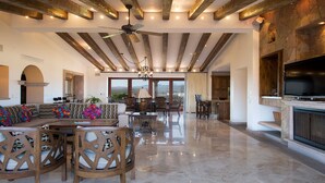 A spacious living area with a high ceiling, exposed beams, a large TV, and a view to the outside.