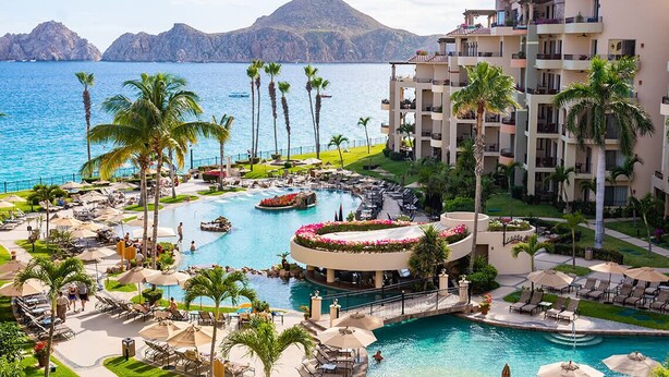 A resort with multiple swimming pools, palm trees, and a view of the sea.