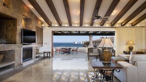 A spacious living area with a stone fireplace, a television, and a view of the ocean.