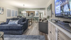 Una sala de estar moderna con un televisor de pantalla plana grande, sofás grises, una zona de cocina y un espacio para comer.