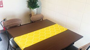 A dining table with a yellow table runner, two chairs, and a potted plant in the background.