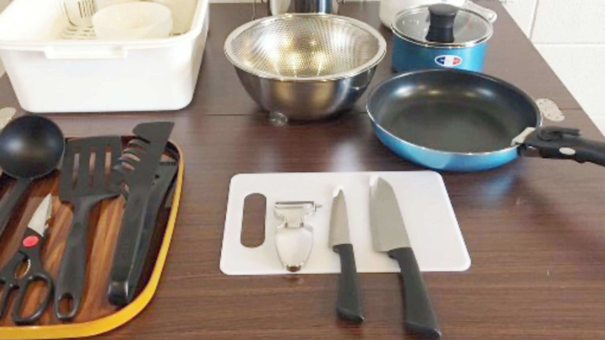 A kitchen counter with various utensils, a colander, a frying pan, and a cutting board.