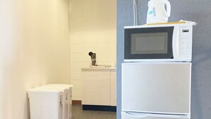 A kitchen with a microwave on top of a refrigerator, a trash bin, and a utensil holder on the counter.