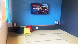 A room with tatami flooring, a blue wall, a mounted TV displaying Netflix content, and a small shelf with a framed picture and a Wi-Fi sign.