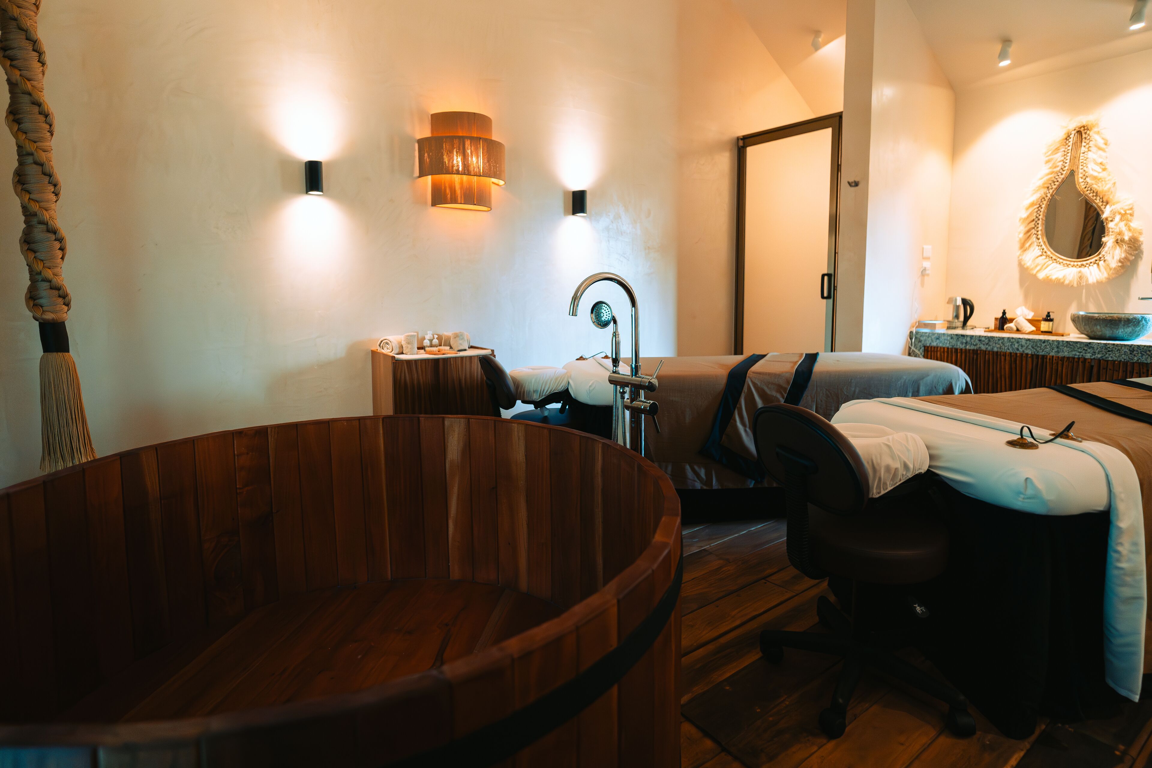 A modern bathroom with a wooden bathtub, a sink with a mirror, and a round wooden chair.