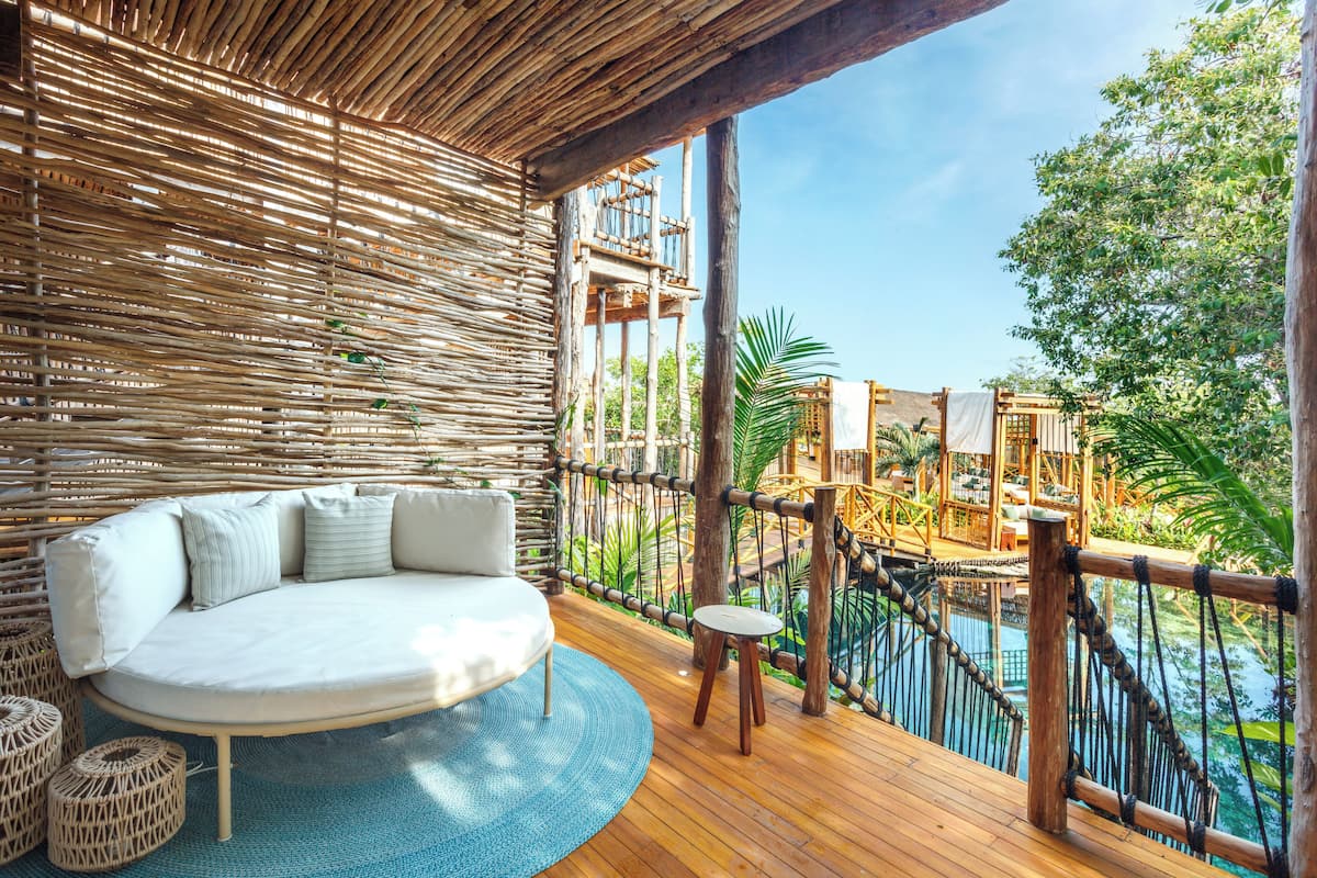 A wooden deck with a cushioned seating area and a view of a pool and jungle.