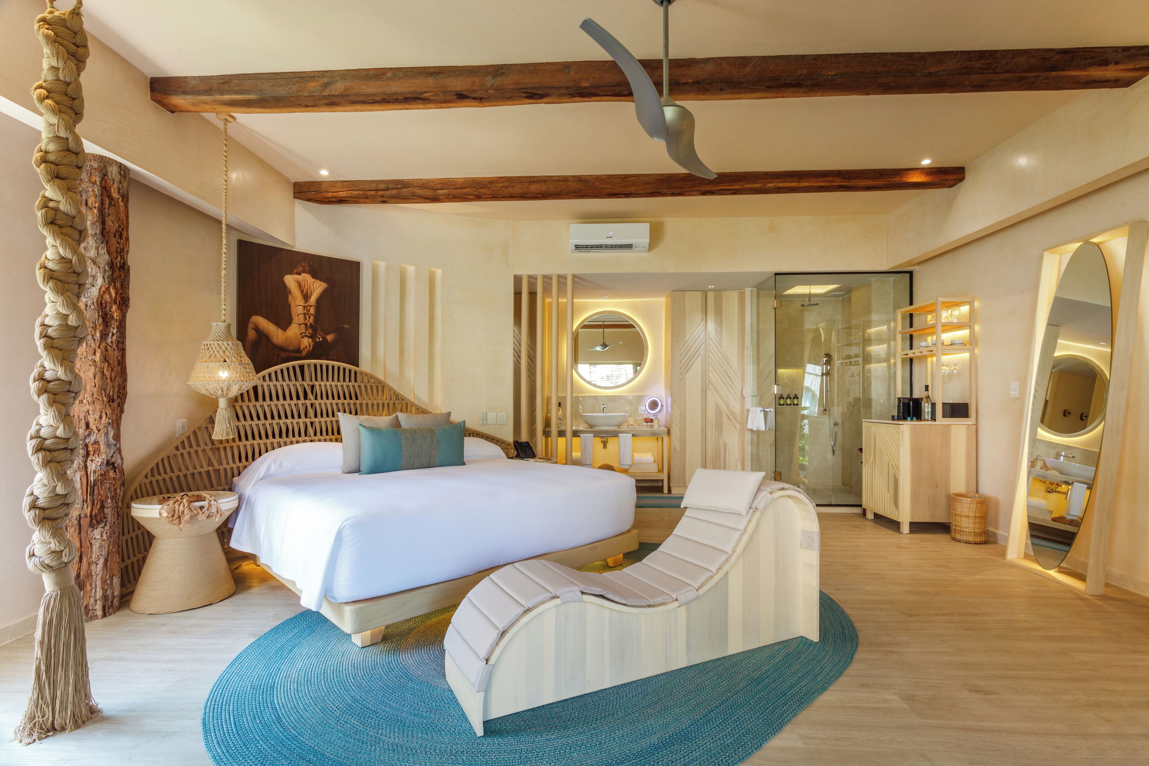 A spacious bedroom with a large bed, a lounge chair, a wooden ceiling, and a bathroom visible through an open door.