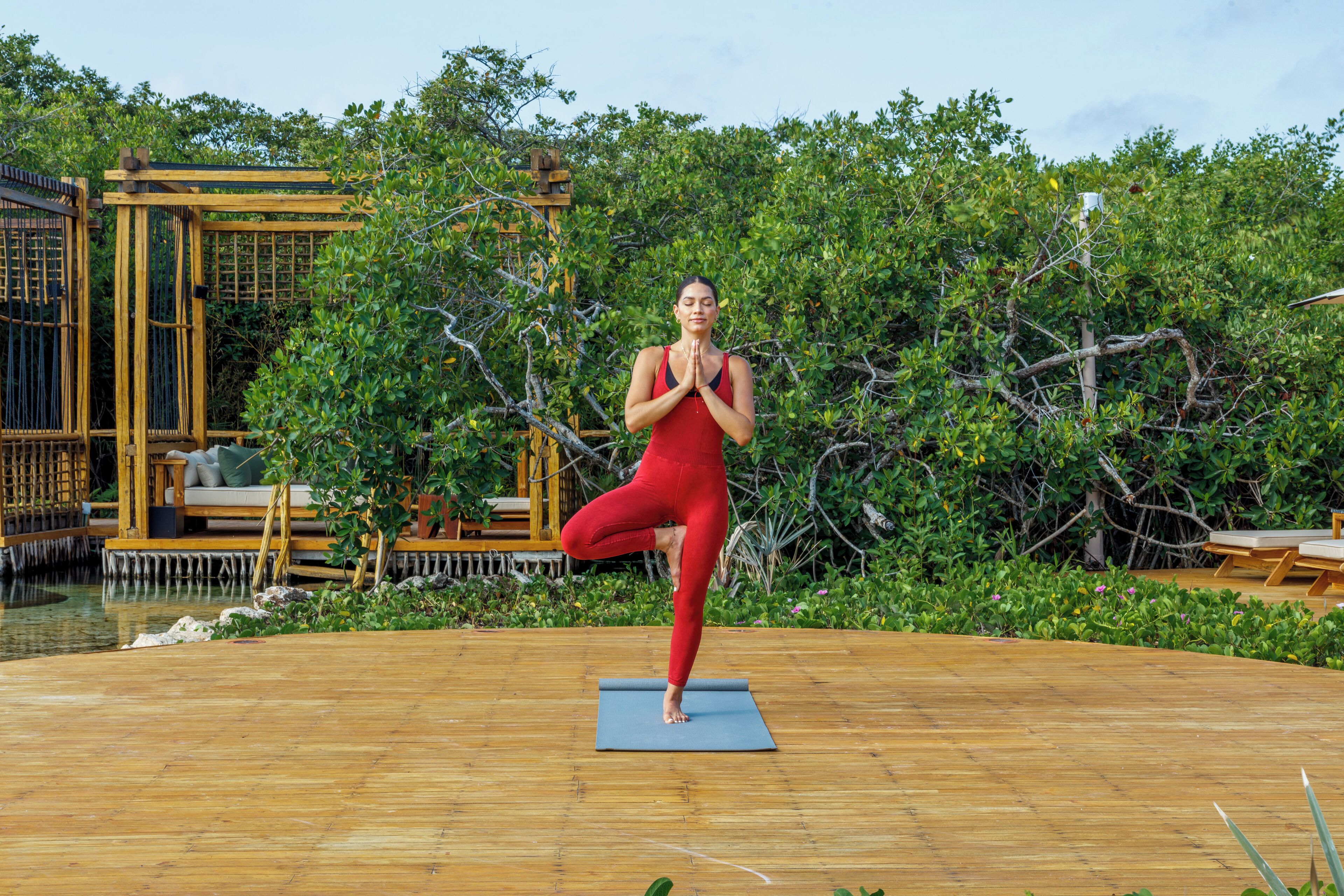 A person performing yoga on a wooden deck with a natural backdrop of trees and a wooden structure.