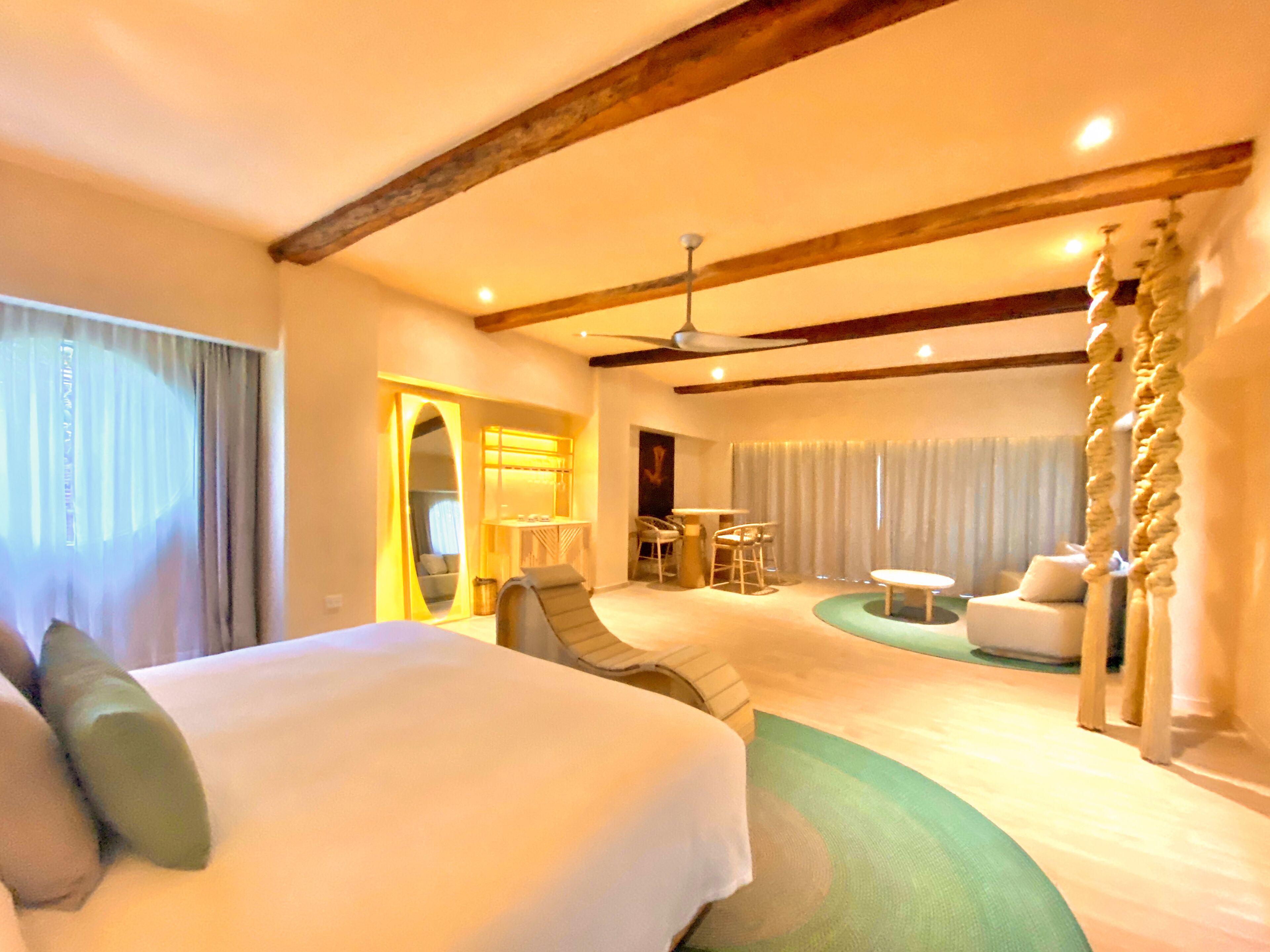 A hotel room with a large bed, a sitting area with chairs, a small table, and a ceiling fan.