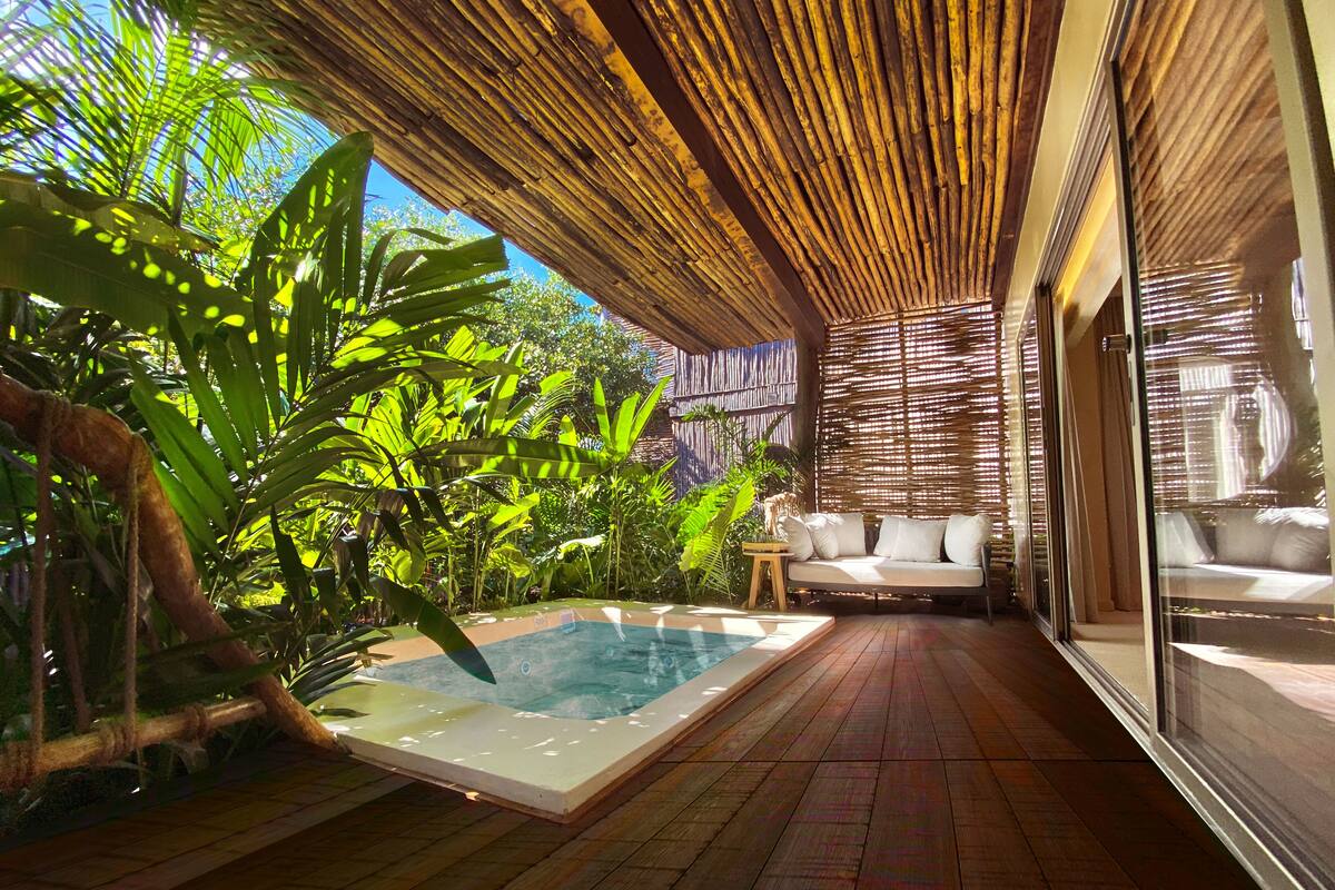 A pool area with a wooden deck, a hot tub, and a sofa with cushions.