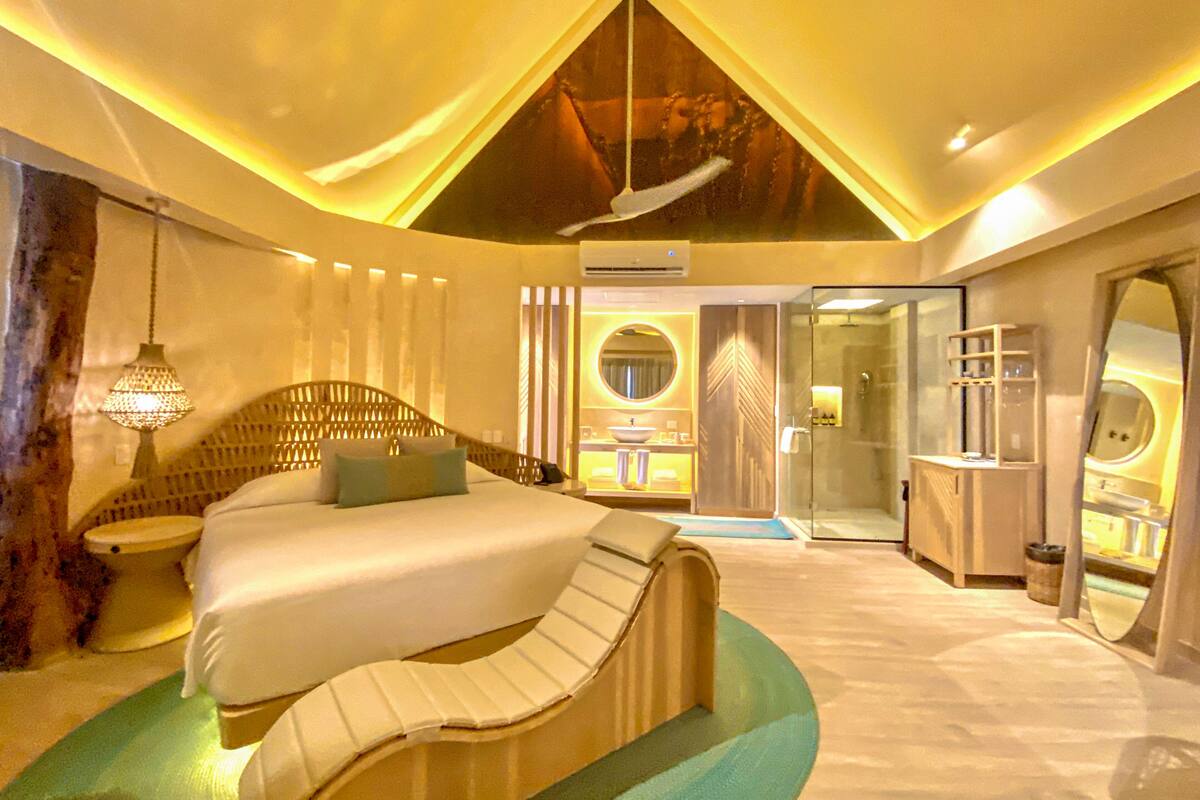 A modern bedroom with a large bed, a glass shower, and a bathroom with a sink and mirror.