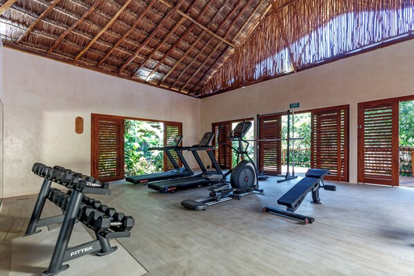 A gym with exercise equipment, a thatched roof, and large windows with shutters.