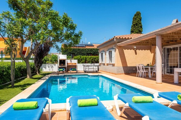 A pool area with lounge chairs, a barbecue, and a covered patio.