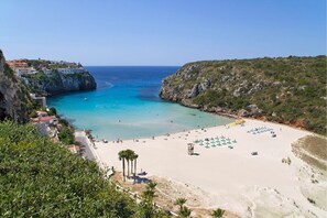 A coastal beach with clear turquoise waters, a sandy shore, and a rocky cliff.
