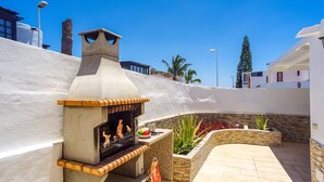 An outdoor barbecue area with a stone oven, surrounded by a white wall and a stone planter with plants. - Villa Fayna by Villa Plus (Puerto del Carmen)