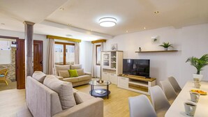 A modern living room with a sofa set, a TV, and a dining area with chairs and a table. - Villa Fayna by Villa Plus (Puerto del Carmen)