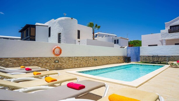 A poolside area with lounge chairs and a lifebuoy on the wall. - Villa Fayna by Villa Plus (Puerto del Carmen)
