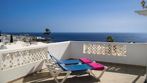 A balcony with two sun loungers, one with a blue cover and the other with a pink cover, overlooking a coastal cityscape and the sea. - Villa Siesta by Villa Plus (Puerto del Carmen)