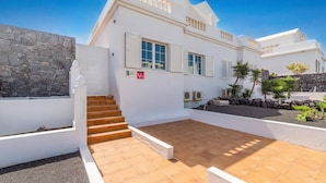 A white villa with a stone wall, a tiled patio, and a staircase leading to the entrance. - Villa Siesta by Villa Plus (Puerto del Carmen)