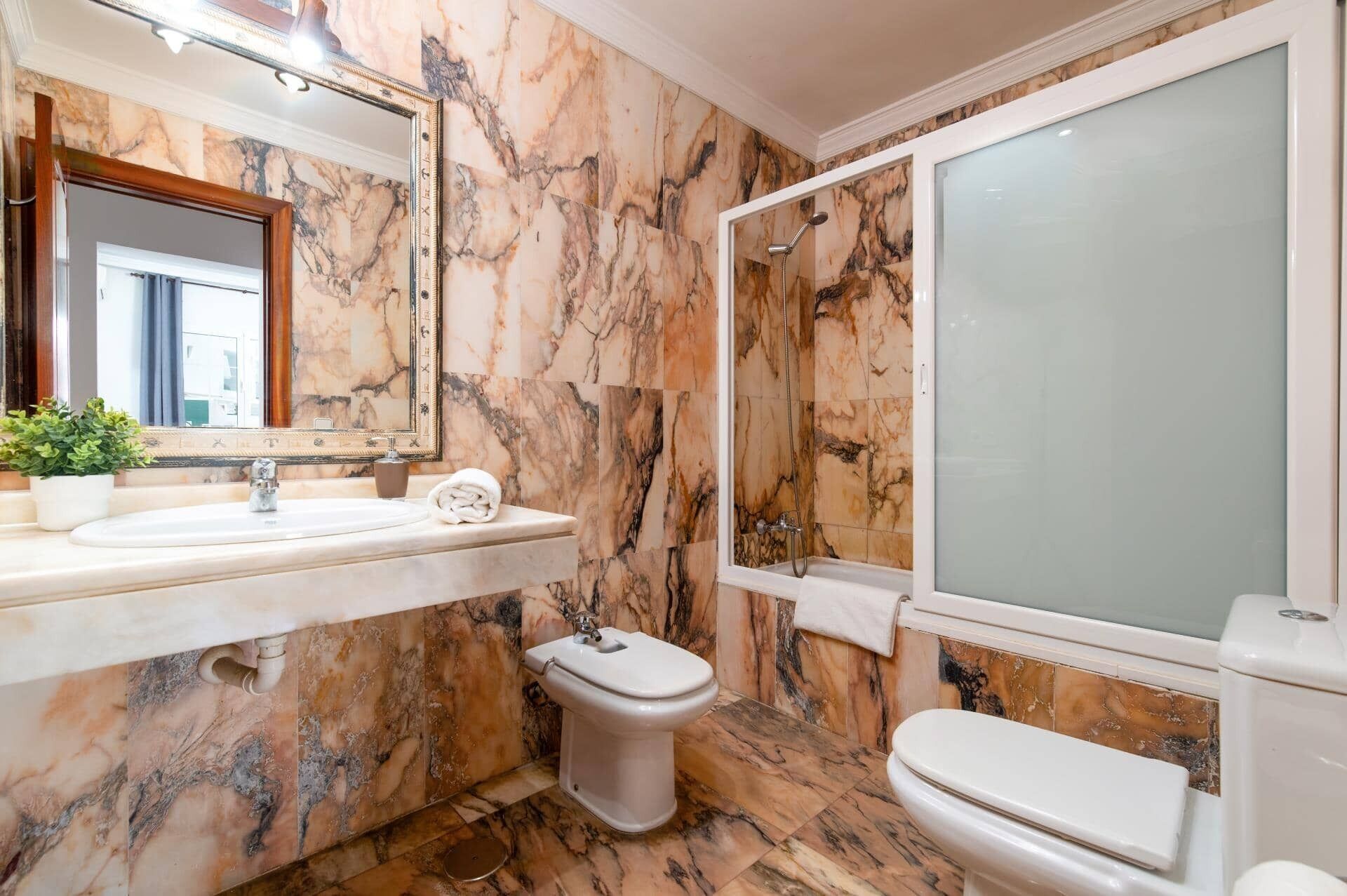 Een badkamer met marmeren wanden, een wastafel, toilet en douche.