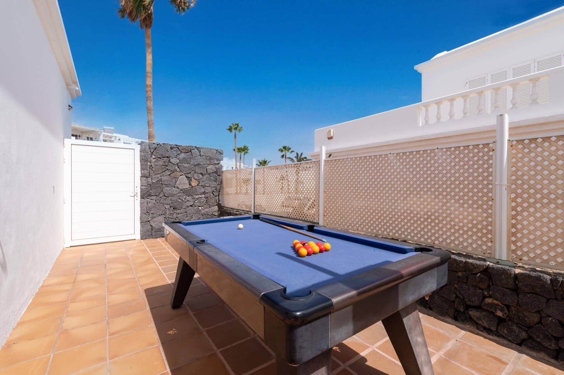 Une table de billard extérieure, avec un mur en pierre et un portail blanc.