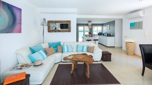 A modern living room with a white sectional sofa, a wooden coffee table, and a kitchen in the background. - Villa Isabella by Villa Plus (Mallorca)