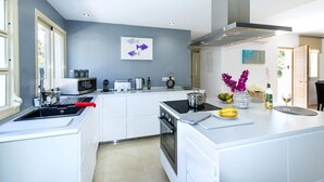 A modern kitchen with white cabinetry, a central island, and a stainless steel range hood. - Villa Isabella by Villa Plus (Mallorca)
