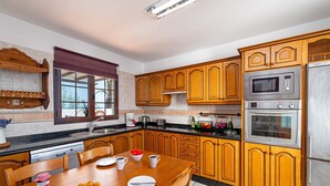 A kitchen with wooden cabinets, a stainless steel refrigerator, a microwave, and an oven. There is a dining table with chairs, a window with a view, and a coffee maker on the counter. - Villa San Marcial by Villa Plus (Tías)