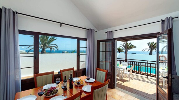 A dining area with a table set for four, overlooking a pool and the sea. - Villa San Marcial by Villa Plus (Tías)