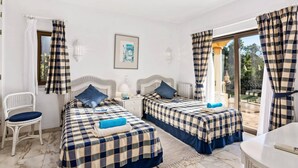 A room with two beds, a chair, a table, and a view of the outdoors. - Villa Racanda by Villa Plus (Carvoeiro)