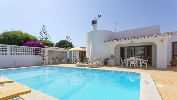 Ein Swimmingpool mit Liegestühlen und eine Terrasse mit Tisch und Stühlen.