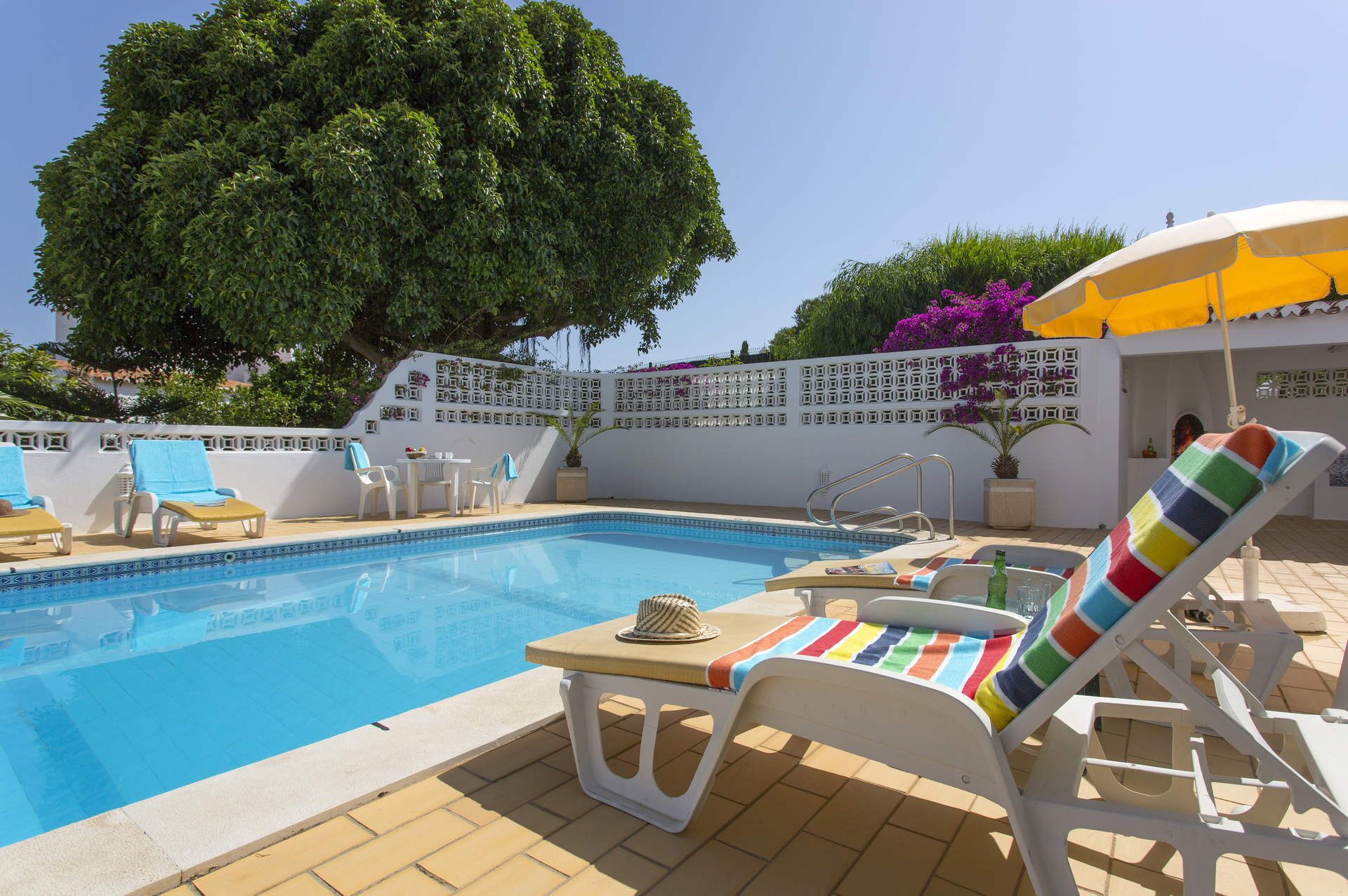 A pool area with lounge chairs, a table, and a yellow umbrella.