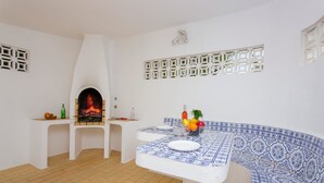Ein Zimmer mit integriertem Kamin, einer gefliesten Sitzbank und einem Tisch mit blau-weiß gemustertem Tischläufer.