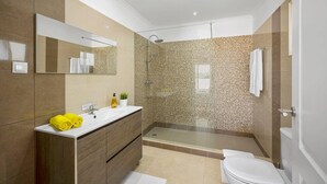 A modern bathroom with a large mirror, a sink with a wooden vanity, a shower with a glass enclosure, and a toilet. - Villa Citrinos by Villa Plus (Almansil)