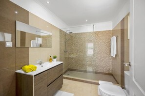 A modern bathroom with a large mirror, a sink with a wooden vanity, a shower with a glass enclosure, and a toilet. - Villa Citrinos by Villa Plus (Almansil)