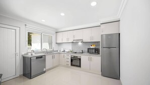 A modern kitchen with white cabinets, stainless steel appliances, and a large window providing natural light. - Villa Citrinos by Villa Plus (Almansil)